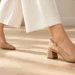 Woman walking in tan leather slingback shoes with a secure heel strap on a light wooden floor.