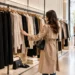 A woman browsing a rack of neutral-toned clothing in a fashion store.